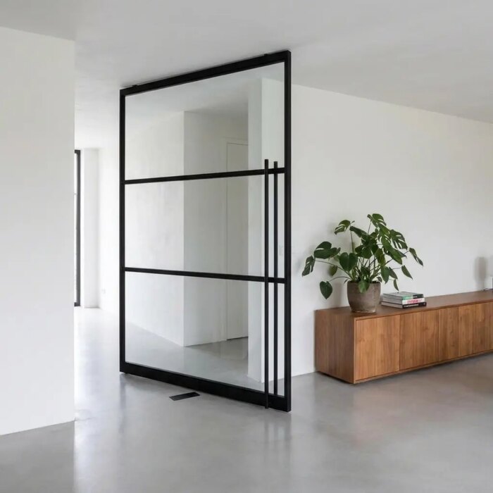 Zwarte stalen taatsdeur met glas, half open in een woonkamer met een lichtgrijze gietvloer Zwarte stalen taatsdeur met glas, half open in een woonkamer met een lichtgrijze gietvloer