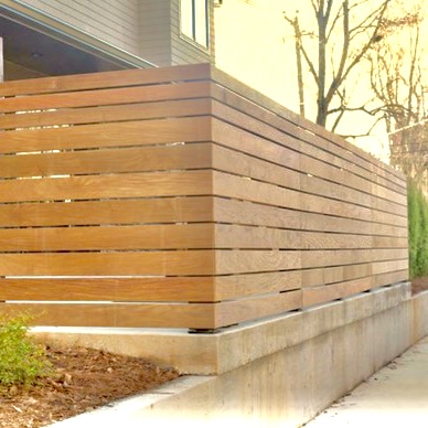 Moderne lamellen schutting van Ip&eacute; hardhout gemonteerd als maatwerk wand op een tuinmuur