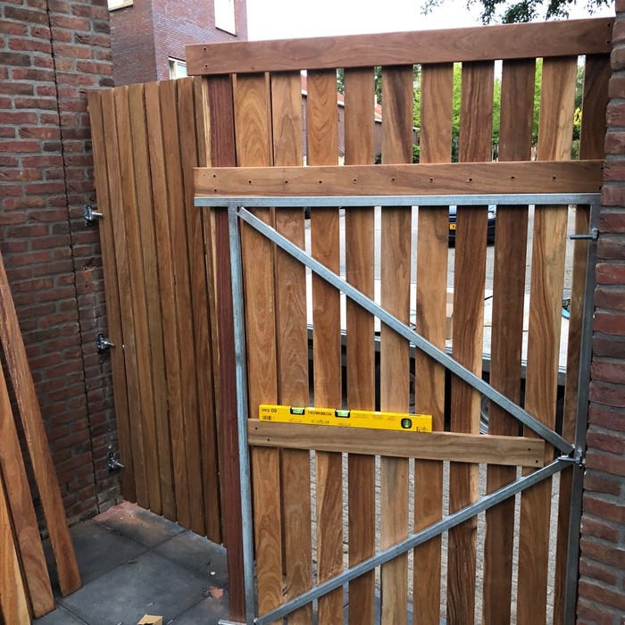 Montage van een hardhouten poort met stalen frame tussen stenen muren