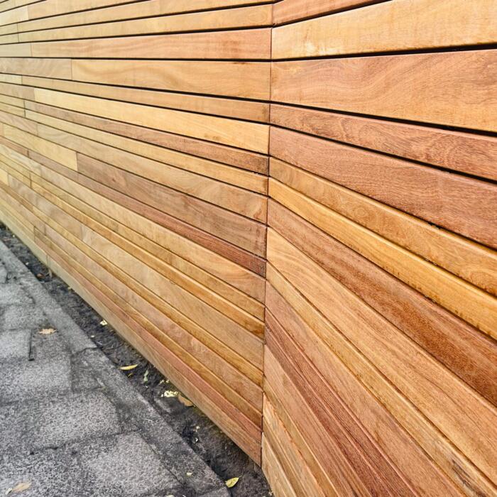 Moderne hoekopstelling van een Ipé variatie schutting waarbij lamellen over de palen vallen