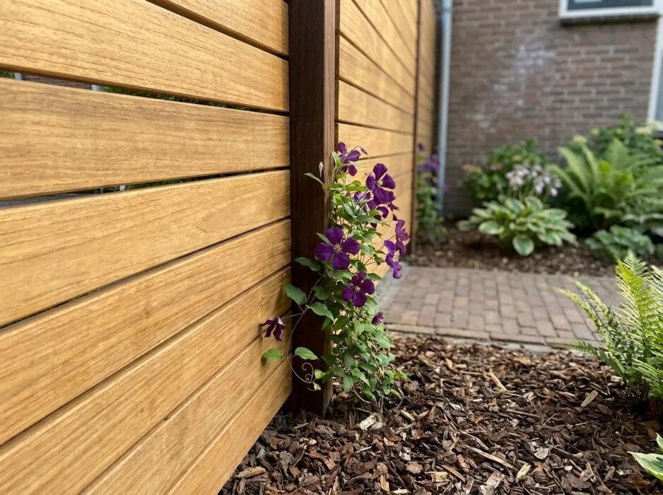 Detail van teak lamellen van 7 cm bij een azobé paal met clematis