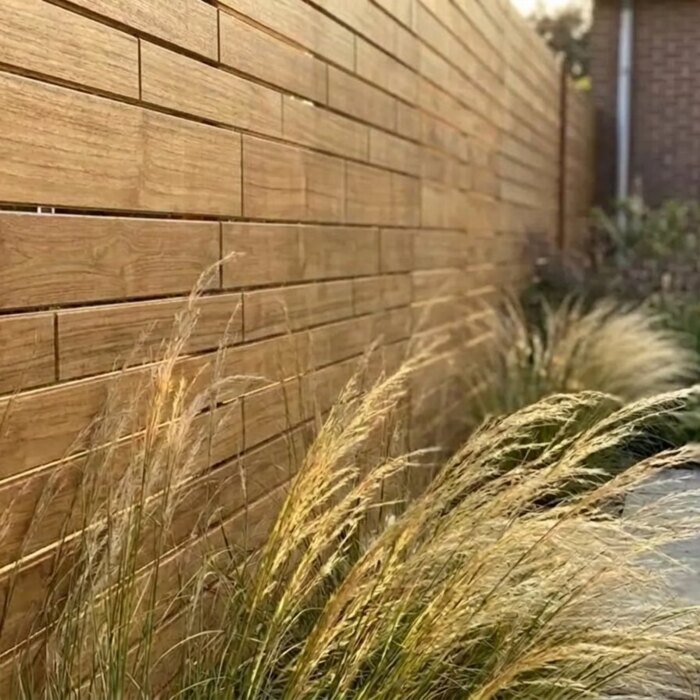 Brede teak schuttingplanken van 9 cm met siergras ervoor Brede teak schuttingplanken van 9 cm met siergras ervoor
