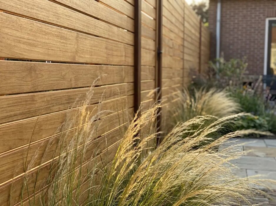 Detail van brede teak lamellen van 9 cm met siergras in de avondzon