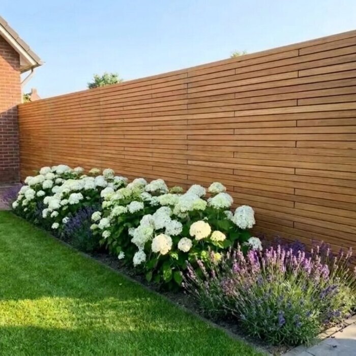 Echte teak schutting met 5 cm lamellen achter een border met witte hortensia's