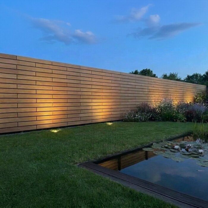 Teak schutting van 7 cm lamellen in de avond, zonder lichtlijnen tussen de lamellen Teak schutting van 7 cm lamellen in de avond, zonder lichtlijnen tussen de lamellen