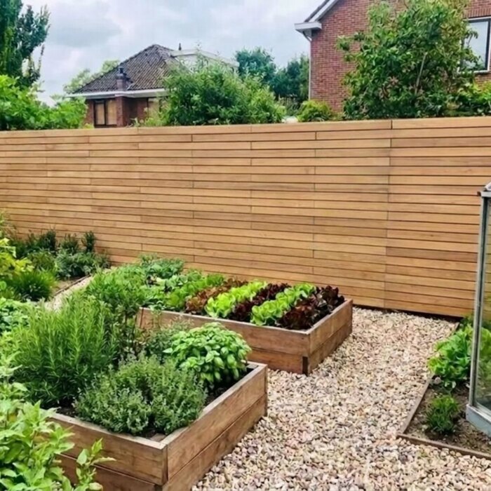 Rond de moestuin: Teak schutting met 7 cm lamellen achter moestuinbakken en een kas
