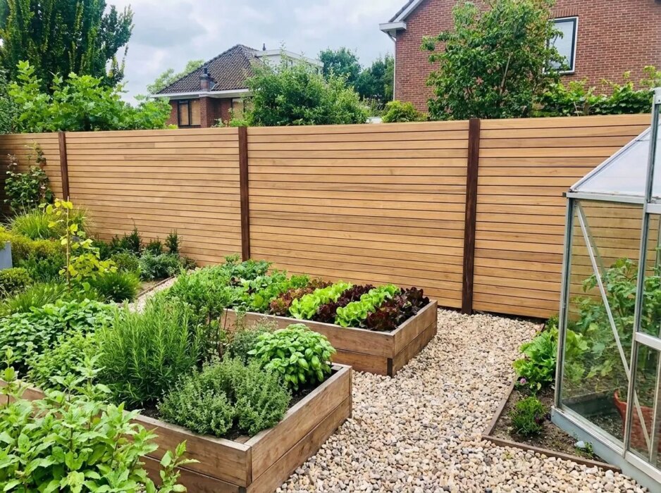 Teak schutting met 7 cm lamellen achter moestuinbakken en een kas