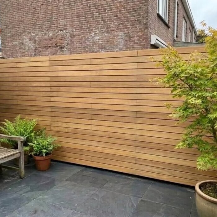 Zichtdichte teak schutting met 9 cm lamellen in een stadstuin met Japanse esdoorn Zichtdichte teak schutting met 9 cm lamellen in een stadstuin met Japanse esdoorn