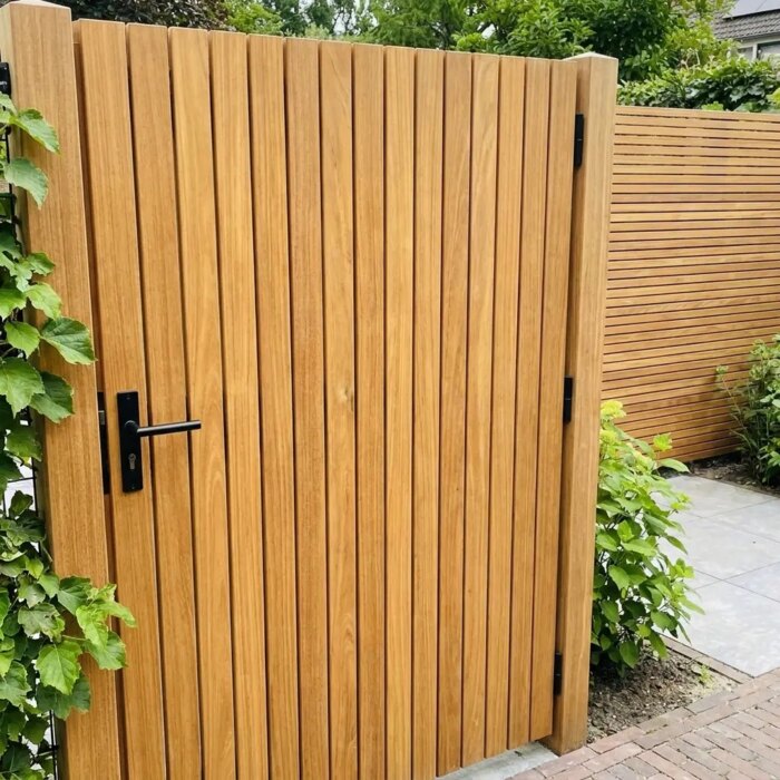 Teak tuinpoort met lamellen van 5 cm naast een klimhortensia, met zwarte deurkruk
