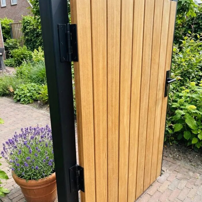 Detail van het zwarte scharnier aan de teak tuinpoort met lamellen van 7 cm