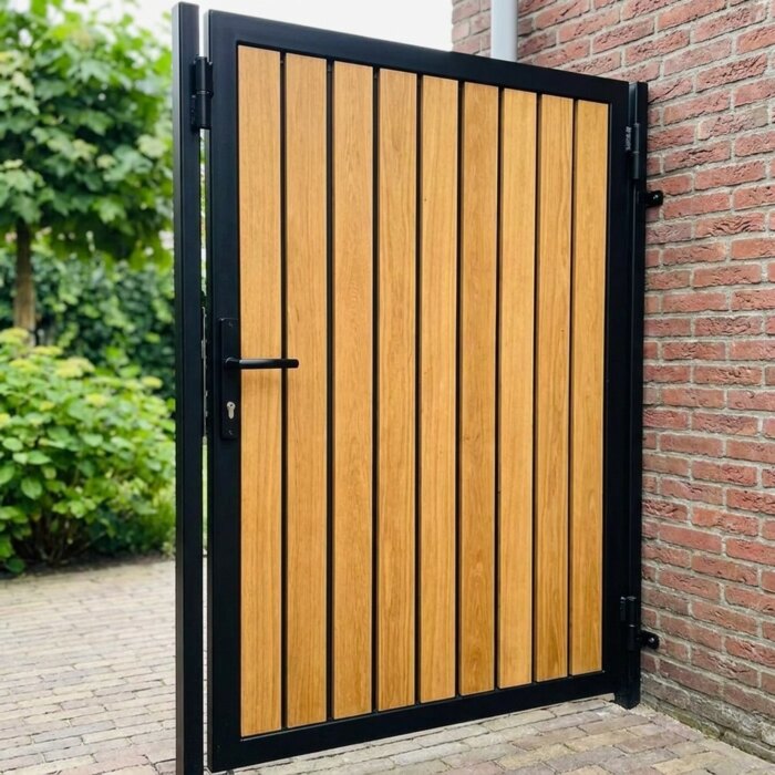 Zwart stalen frame en scharnier van een teak tuinpoort, naast een dikke poortpaal Zwart stalen frame en scharnier van een teak tuinpoort, naast een dikke poortpaal