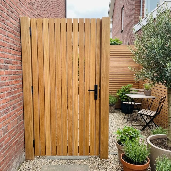 Teak tuinpoort van 9 cm lamellen in een stadstuin met bakstenen muur en olijfboom