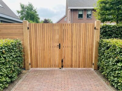 Dubbele teak tuinpoort aan het eind van een oprit met gebakken klinkers