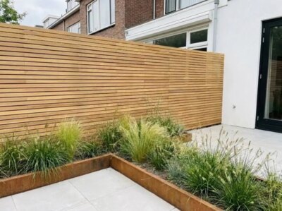 Teak schutting met lamellen van 5 cm in een achtertuin met cortenstalen plantenbak
