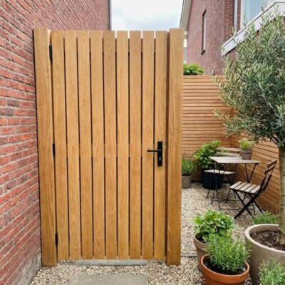 Teak tuinpoort van 9 cm lamellen in een stadstuin met bakstenen muur en olijfboom