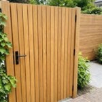 Teak tuinpoort met lamellen van 5 cm naast een klimhortensia, met zwarte deurkruk