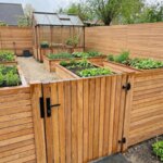 Teak tuinpoort van 7 cm lamellen in een teak schutting rond een moestuin met kas