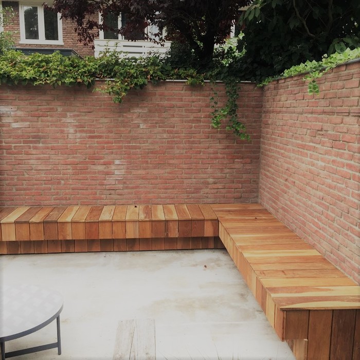 Luxe Ipé hardhouten hoekbank gemonteerd langs een stenen tuinmuur